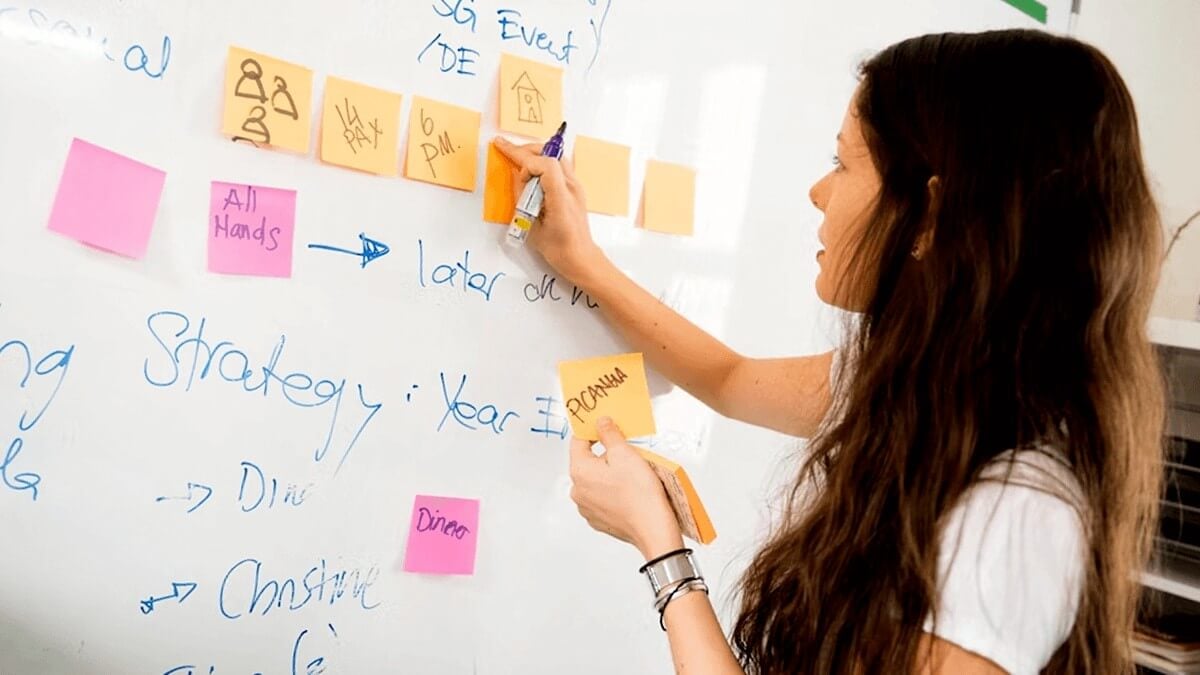 a female designer add a sticky note to a whiteboard