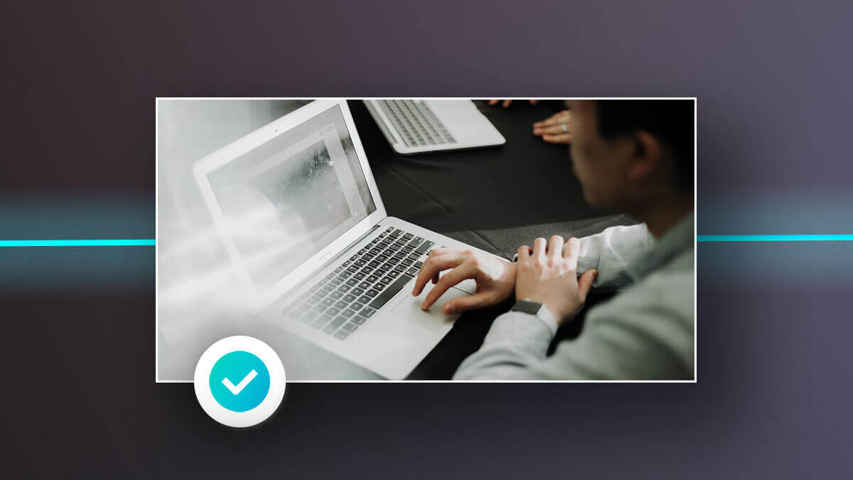 Person using a laptop at a table, with a blue checkmark icon in the corner.