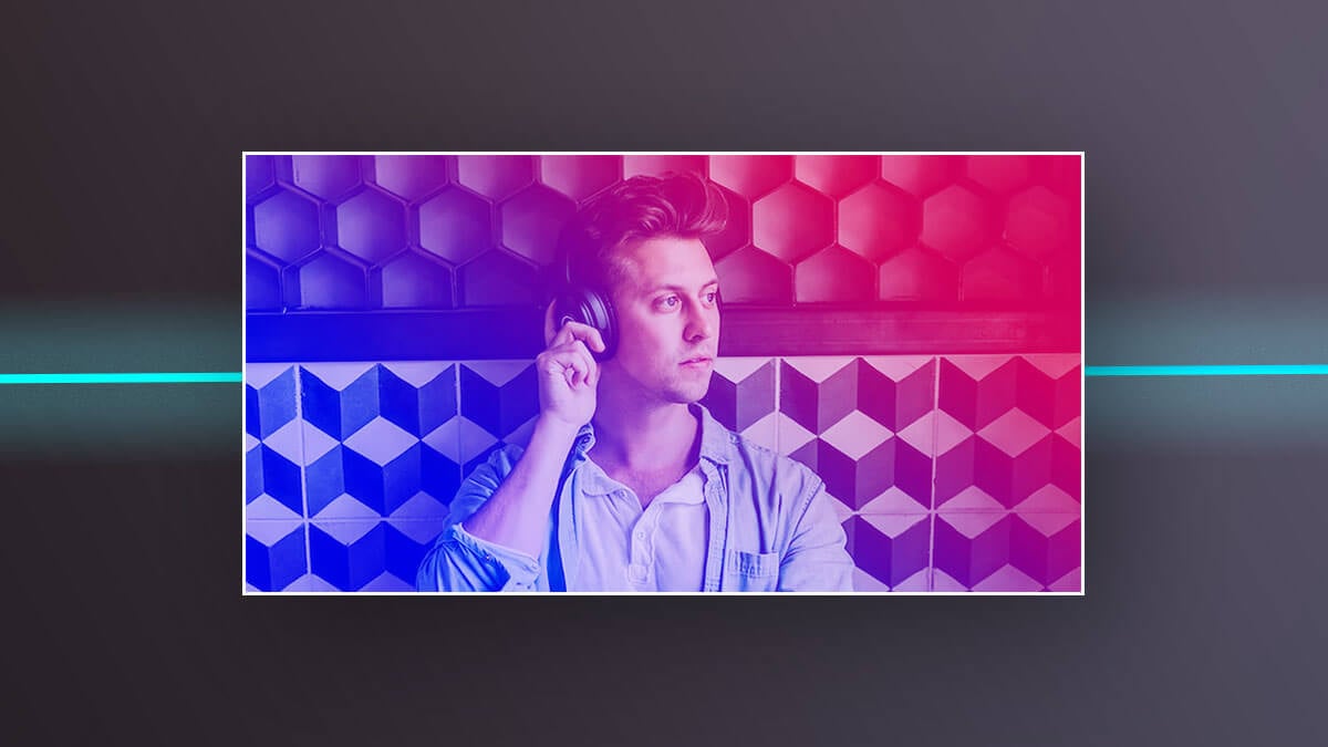 Man wearing headphones against a geometric wall with pink and blue lighting.