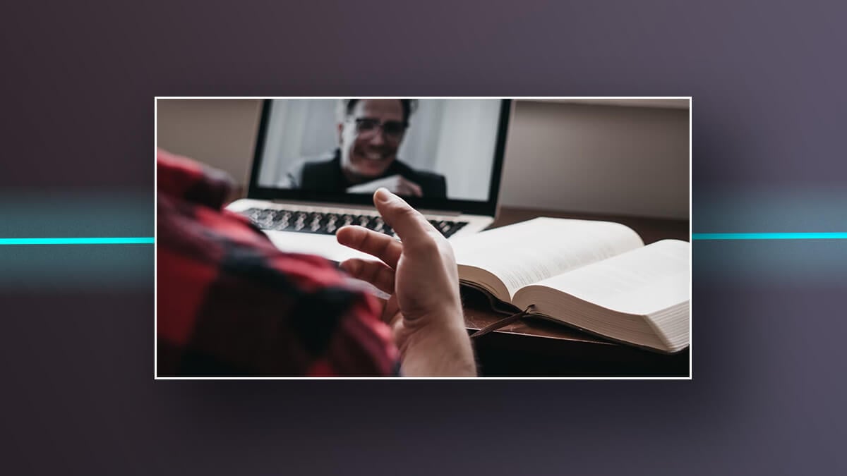 Person video chatting on a laptop beside an open book.