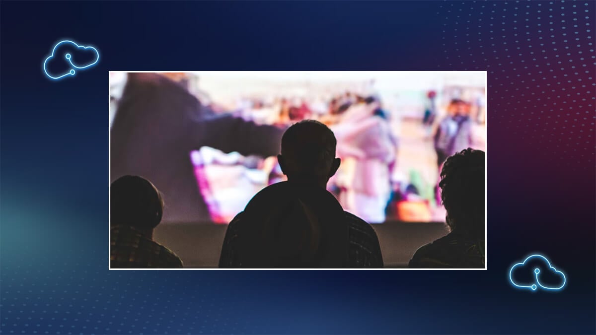 Silhouetted audience watching a large projected video screen.