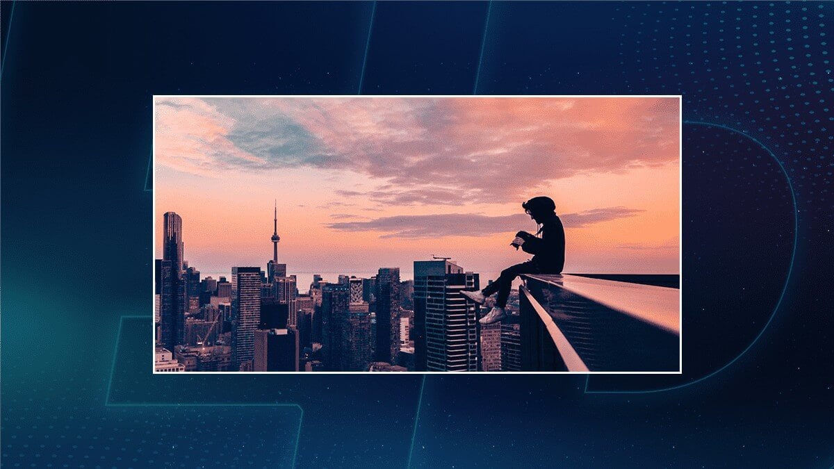 Silhouette of a person sitting on a rooftop ledge above a city skyline at sunset.