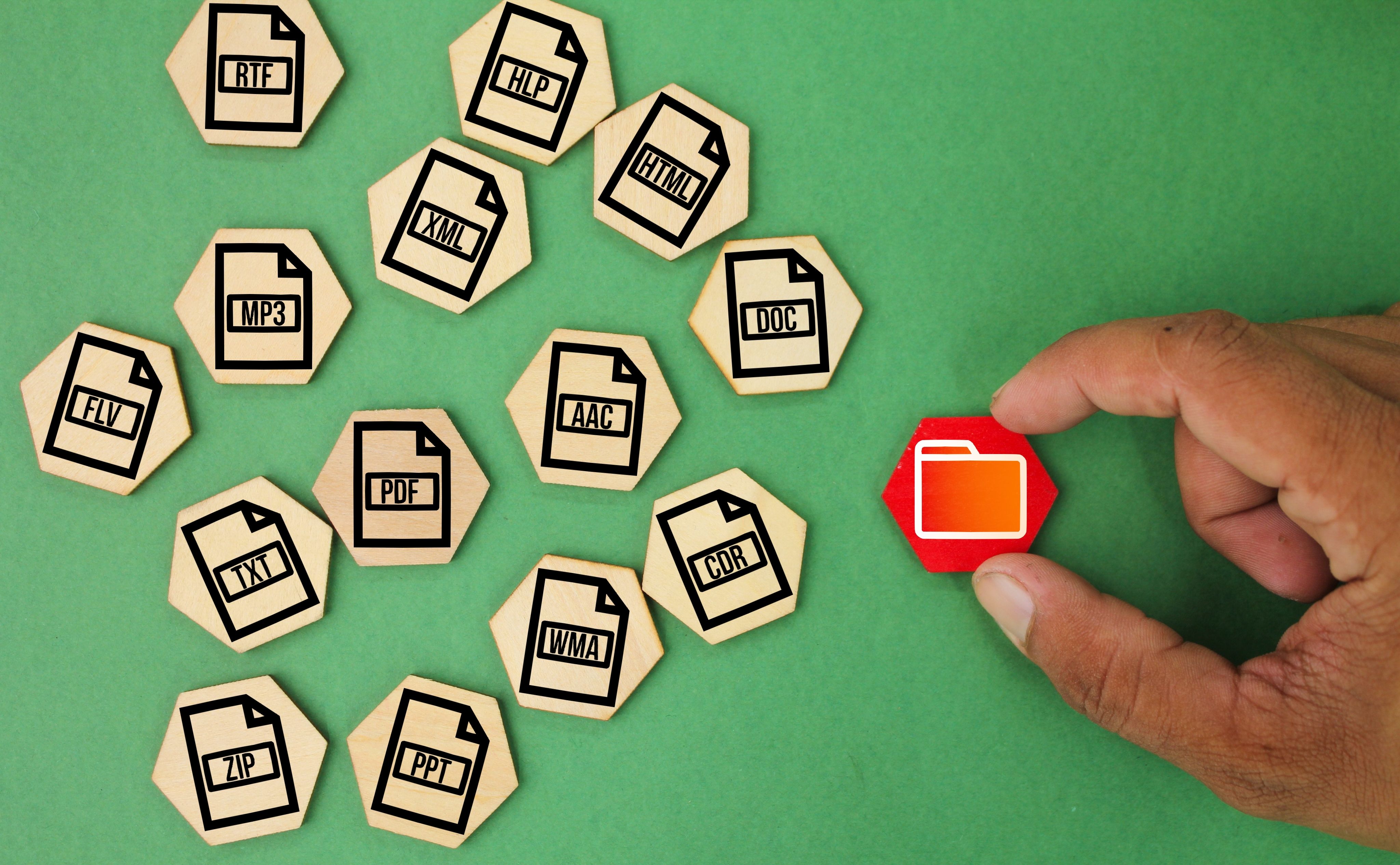 Hand placing a red folder icon among wooden file-type tiles on a green background.
