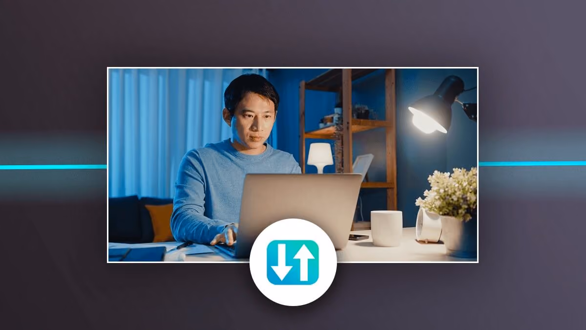Man working on a laptop at a desk, with a file transfer icon below.