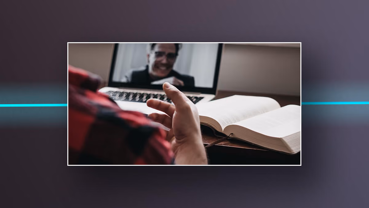 Person video chatting on a laptop beside an open book.