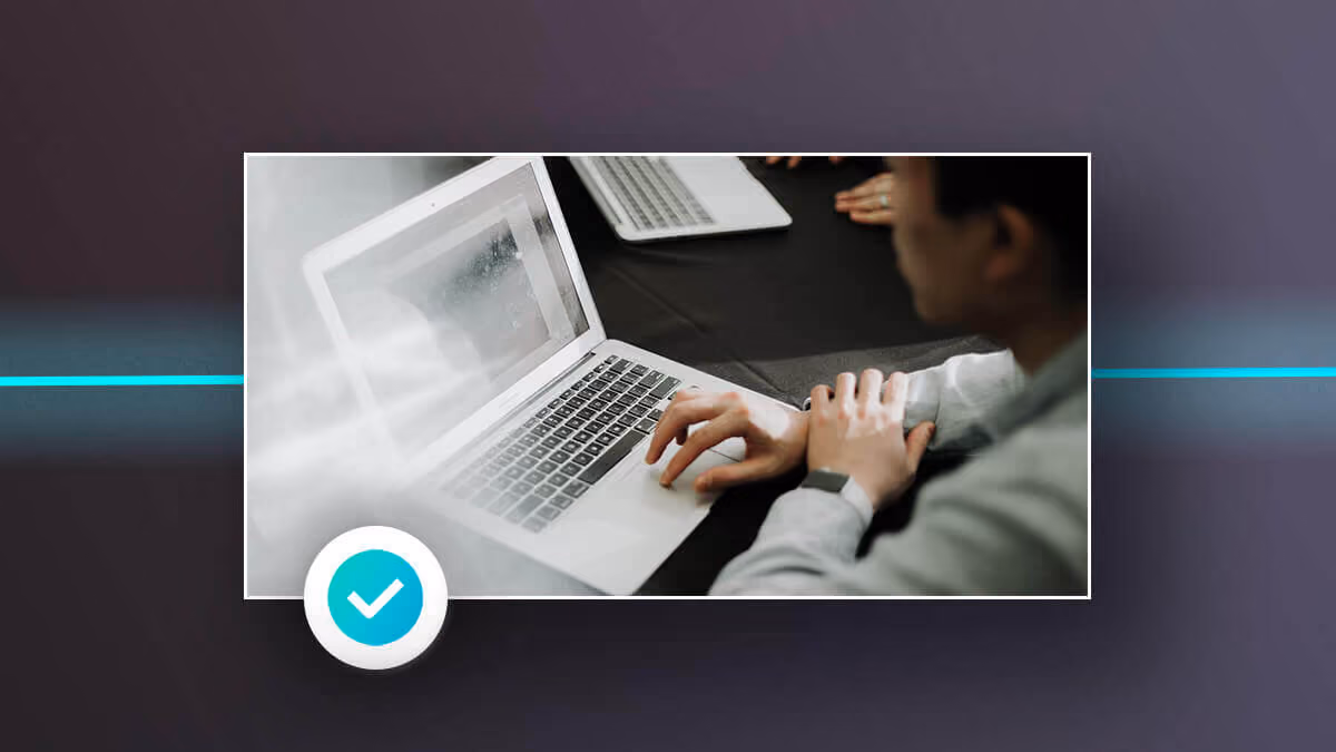 Person using a laptop at a table, with a blue checkmark icon in the corner.