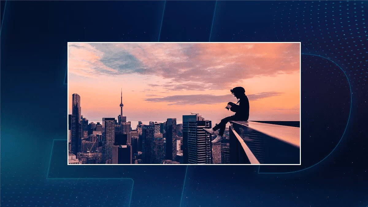 Silhouette of a person sitting on a rooftop ledge above a city skyline at sunset.