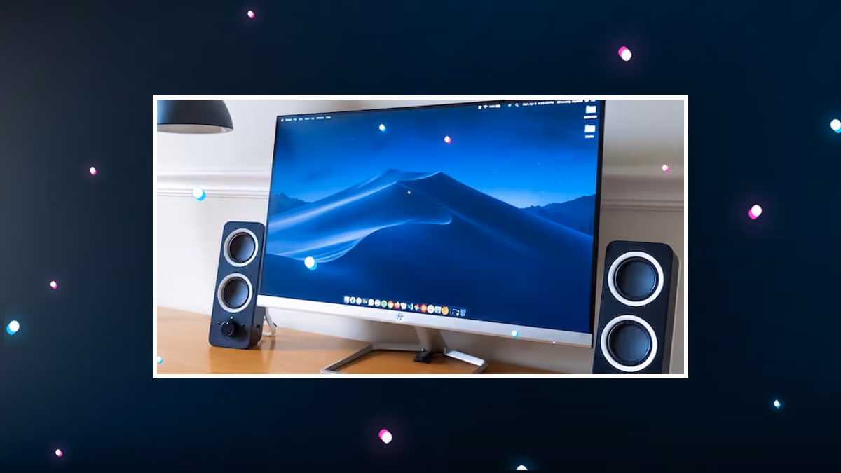 Computer monitor with desktop wallpaper, flanked by two speakers, shown on a dark graphic background.